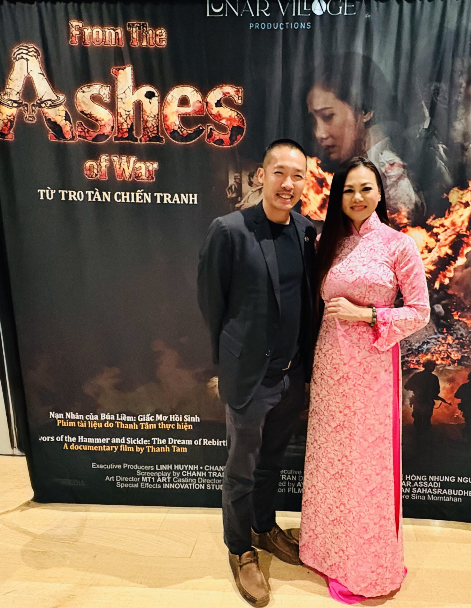 Di Tran stands with director Thanh Tam, wearing a pink áo dài, in front of the From the Ashes of War film banner at the Louisville screening.